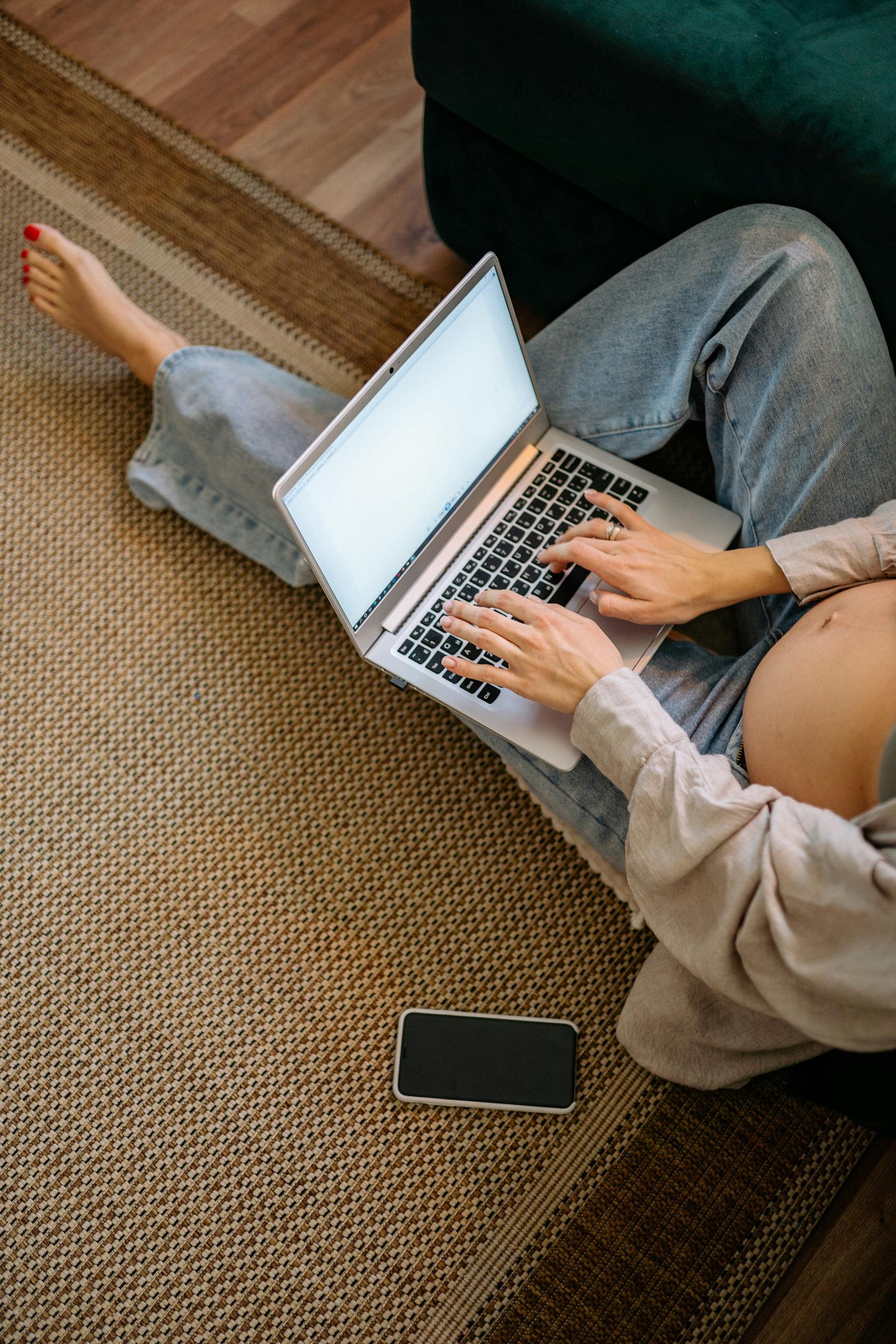 Pregnant woman sitting on carpet using a laptop at home, embracing technology.